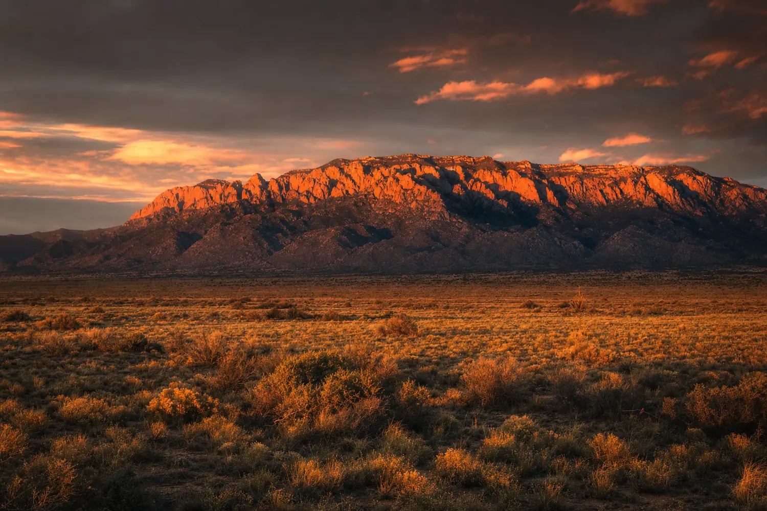 The Sandia Mountains glowing red above the Albuquerque high desert at sunset.